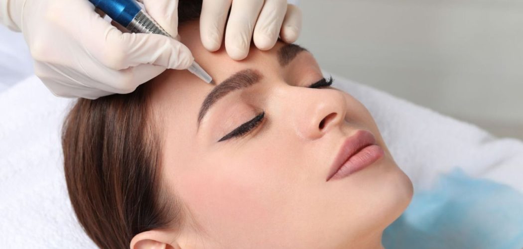 Close-up of woman receiving microblading treatment on eyebrows by a gloved professional with a blue tool
