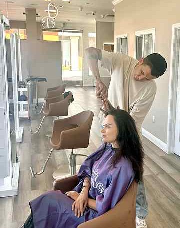 Stylist cutting layers into a woman's hair at Gloss & Glam in Los Angeles